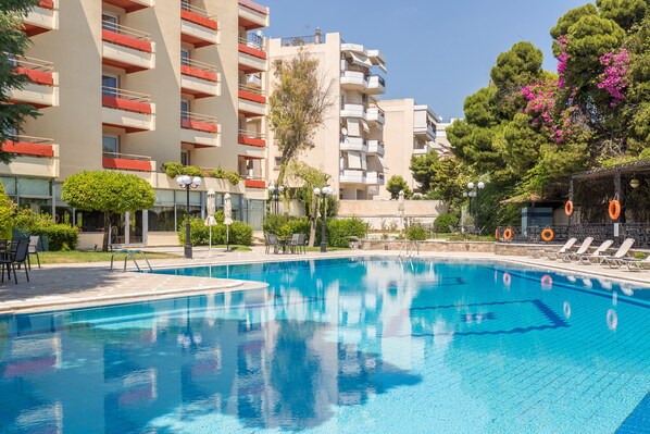Una piscina con sillas de descanso y un edificio con balcones al fondo.