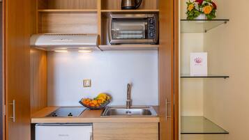 A compact kitchen with a built-in toaster oven, a coffee maker, and a fruit bowl on the counter.
