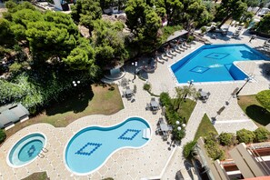 Vista aérea de un complejo turístico con dos piscinas, zonas de estar al aire libre y exuberante vegetación.