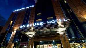 El exterior del Hotel Mercure con un llamativo letrero iluminado, amplias ventanas y un diseño arquitectónico moderno.