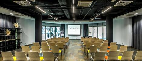A conference room with rows of chairs, a projector screen, and a large window with a view of the street.