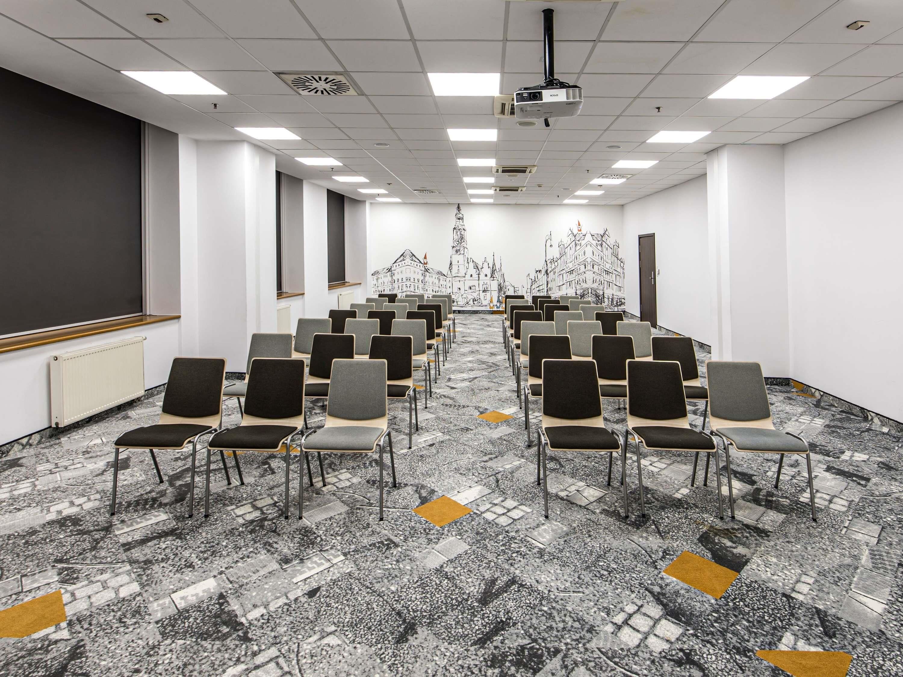 A conference room with rows of chairs, a projector, and a large screen.