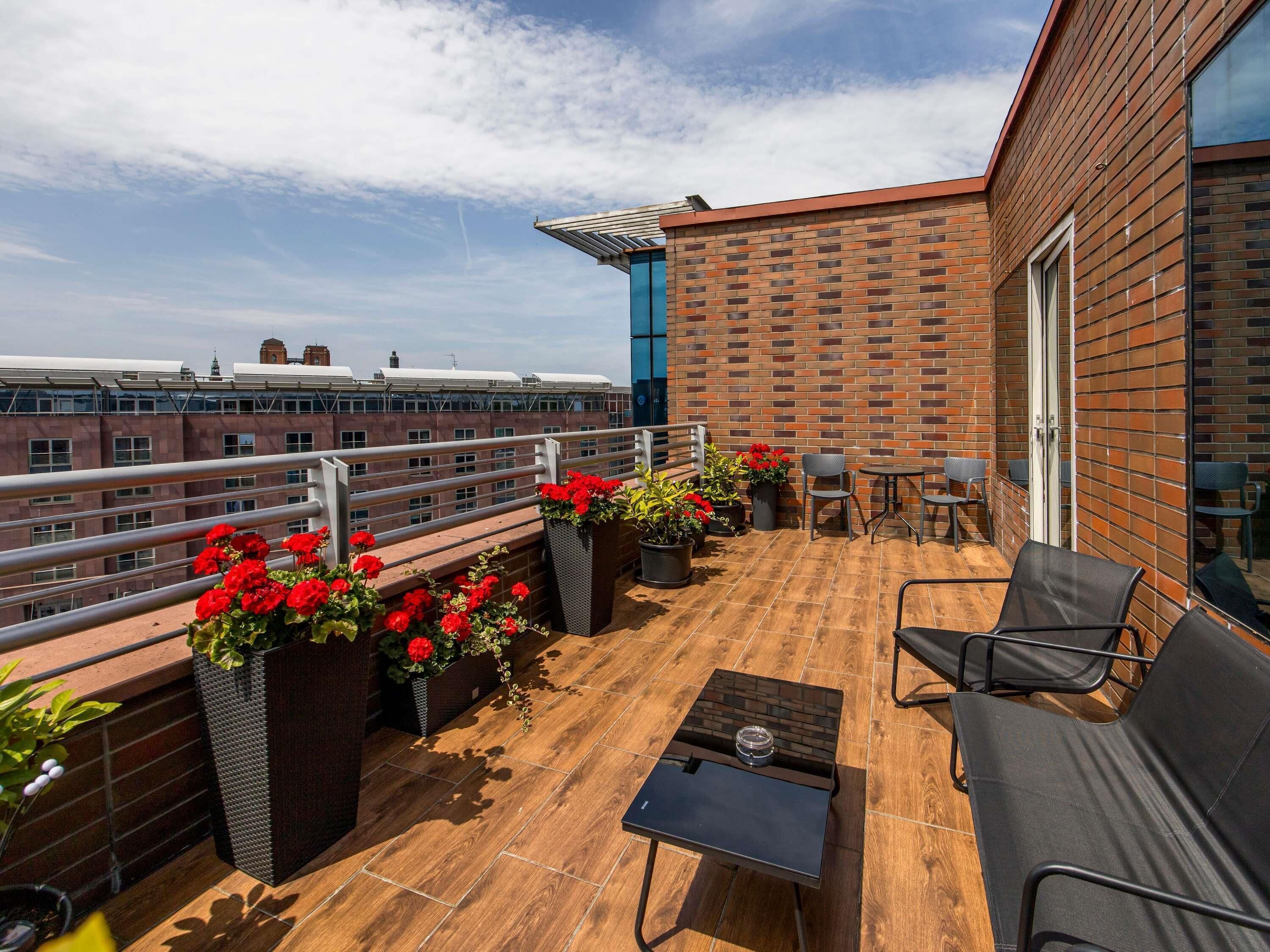 Une terrasse sur le toit, avec un mur en briques, des plantes en pot, des sièges d’extérieur et une vue sur les bâtiments.