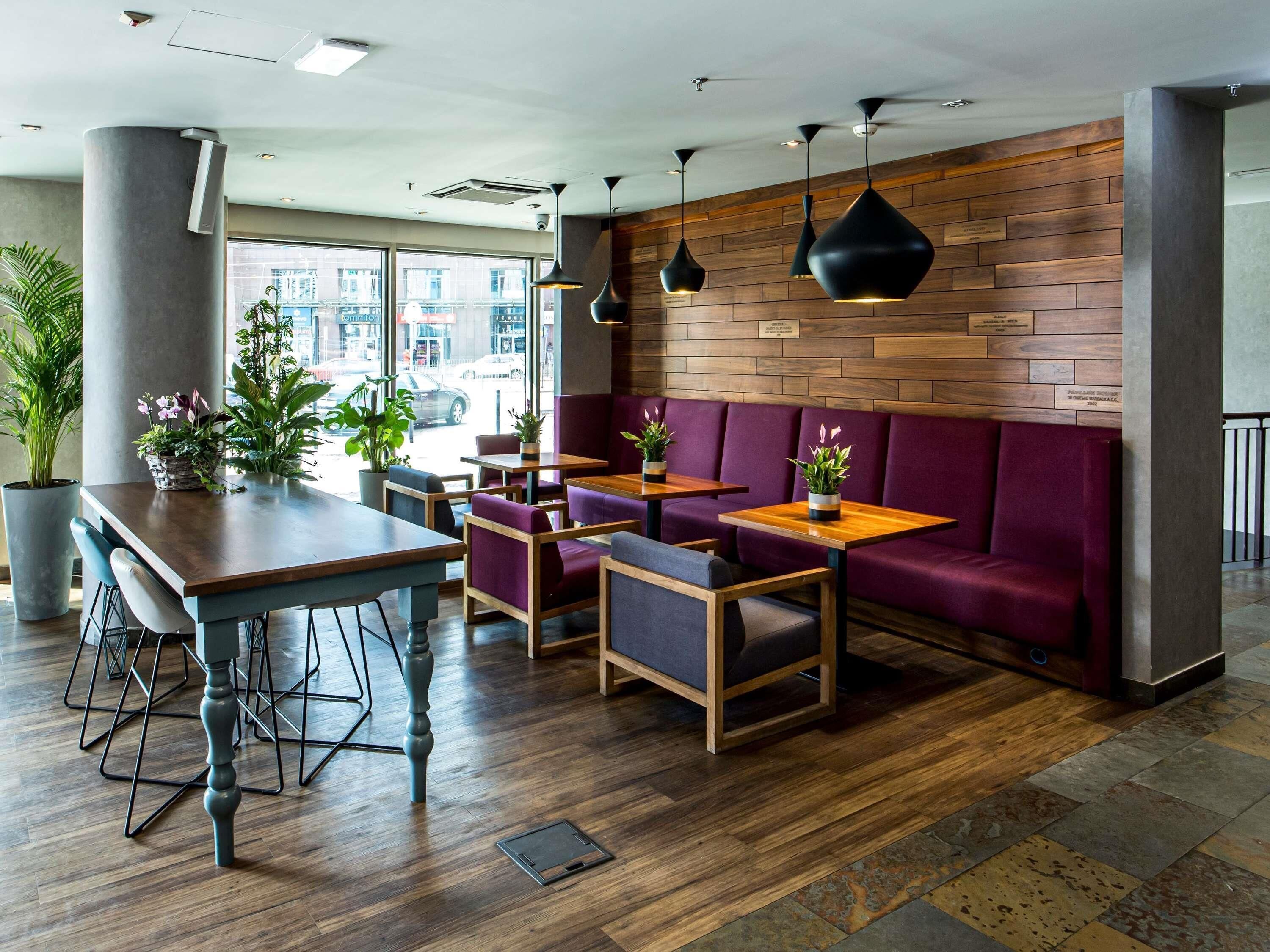 A modern restaurant interior with wooden walls, purple seating, and potted plants.