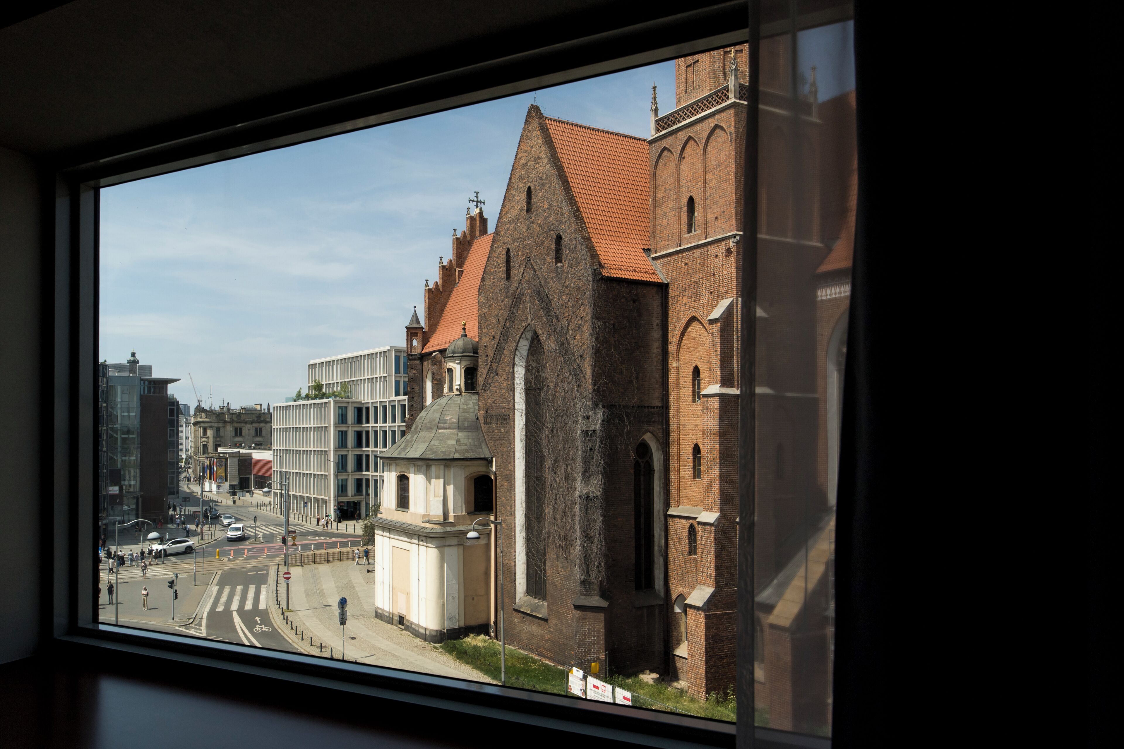A view of a cityscape through a window, including a prominent church with a red roof and a modern building with a glass facade.
