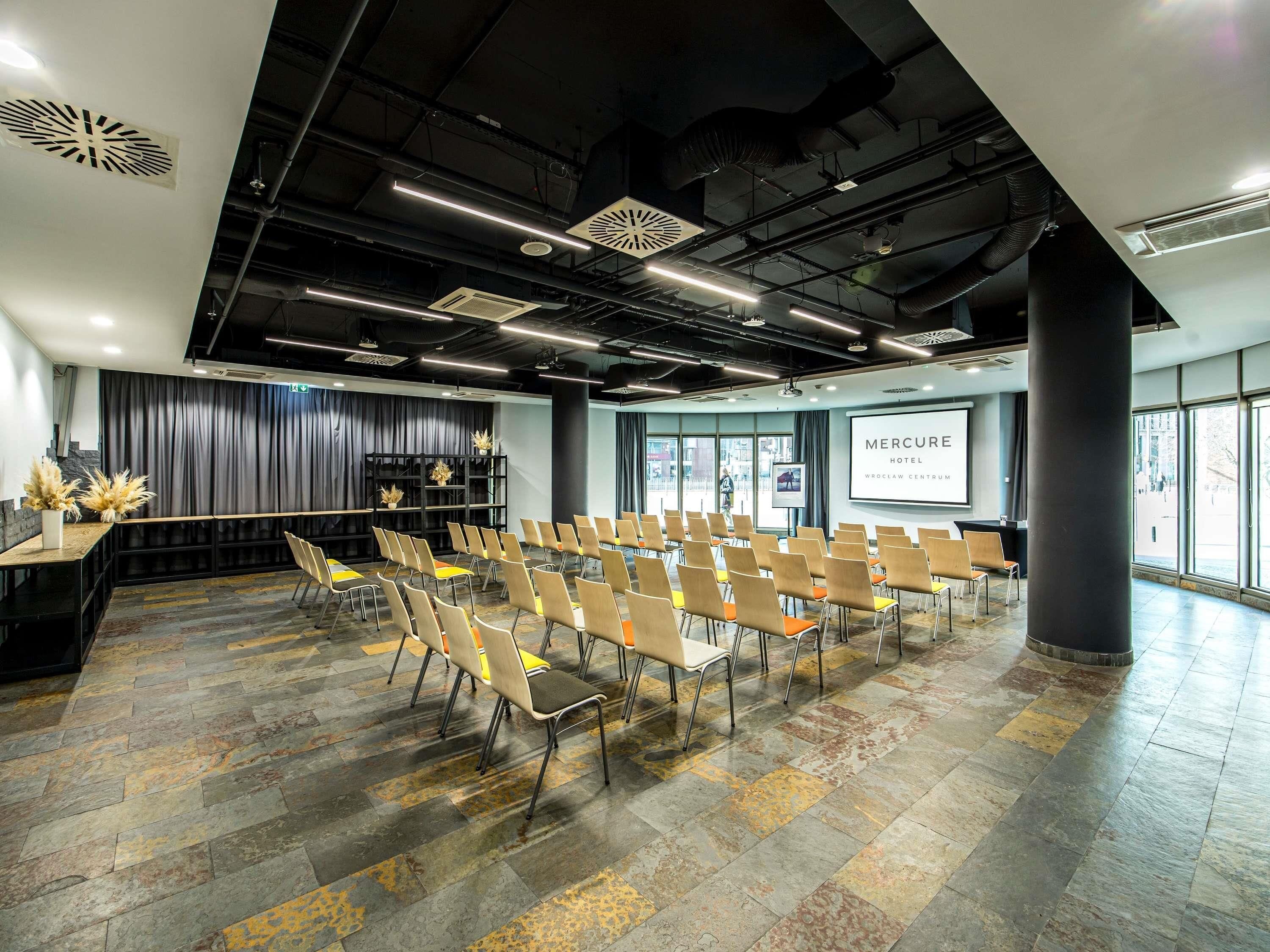 Une salle de conférence avec des rangées de chaises, un écran de projection et une grande fenêtre.