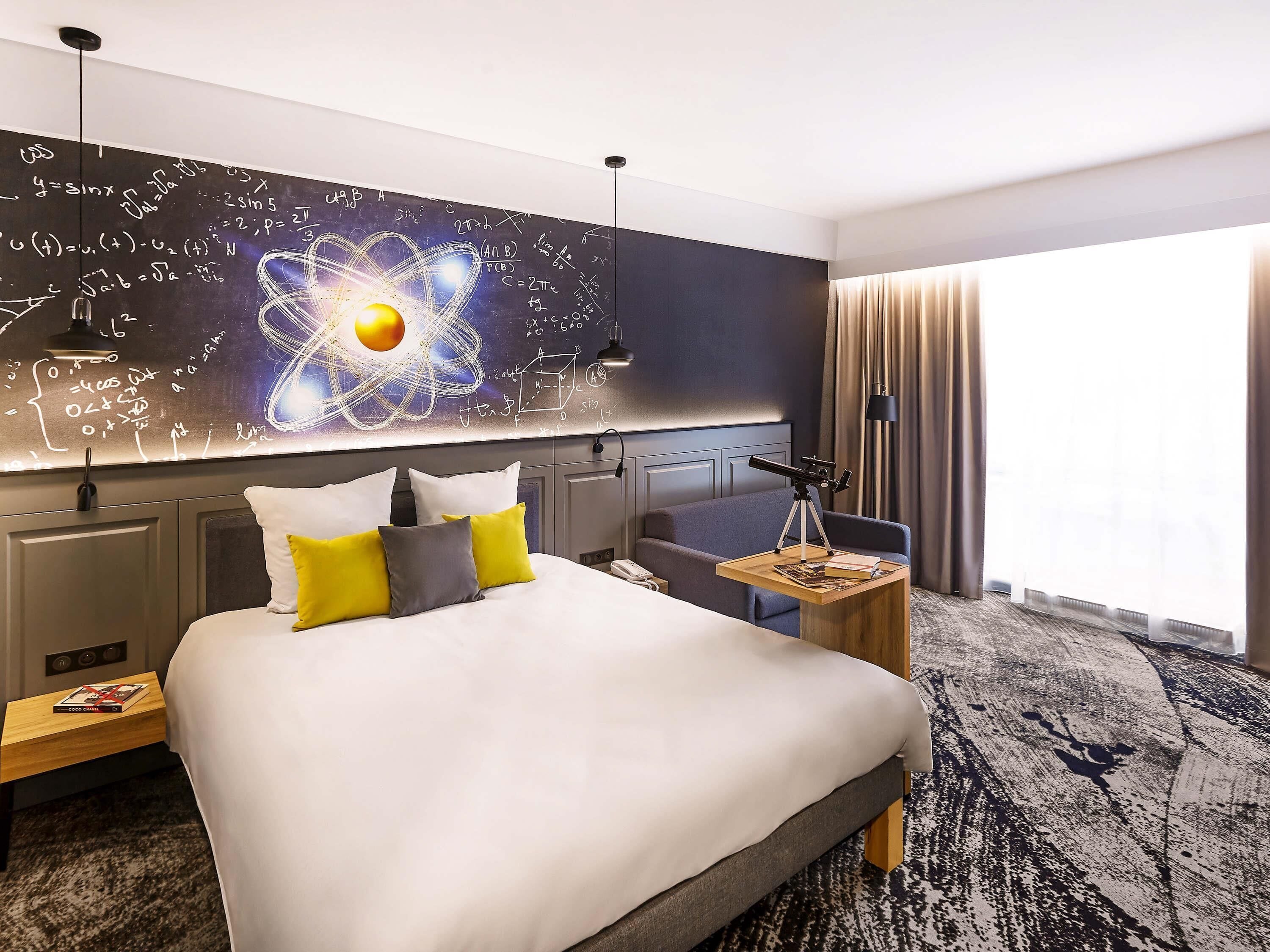 A hotel room with a large bed, a desk with a lamp, a telescope, and a wall with mathematical equations.