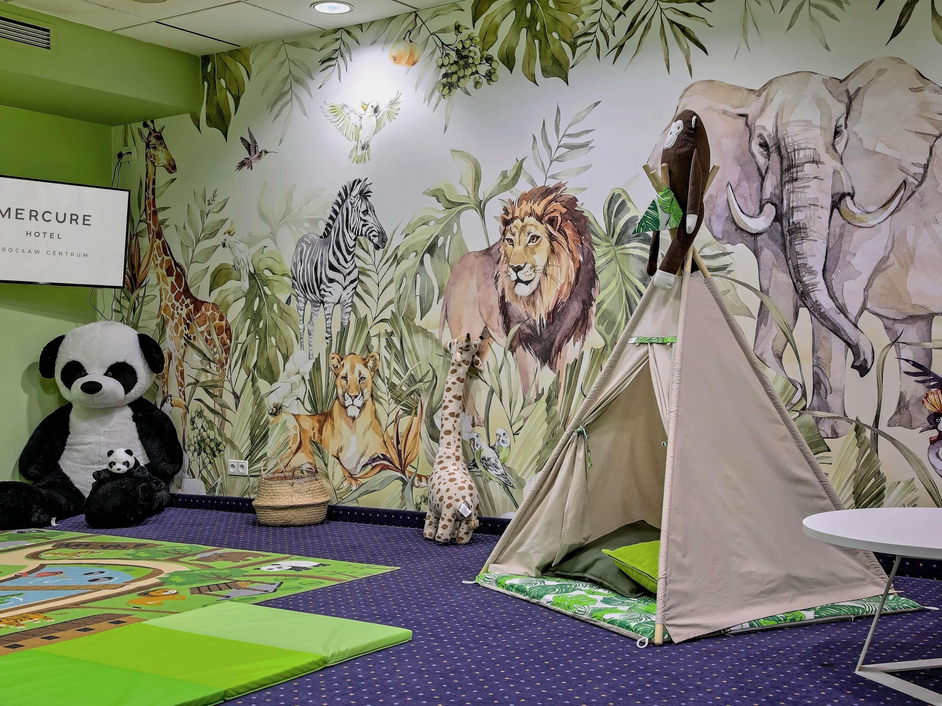 A room with a mural of animals, a tent, a plush panda, and a sign reading 'Mercure Hotel'.