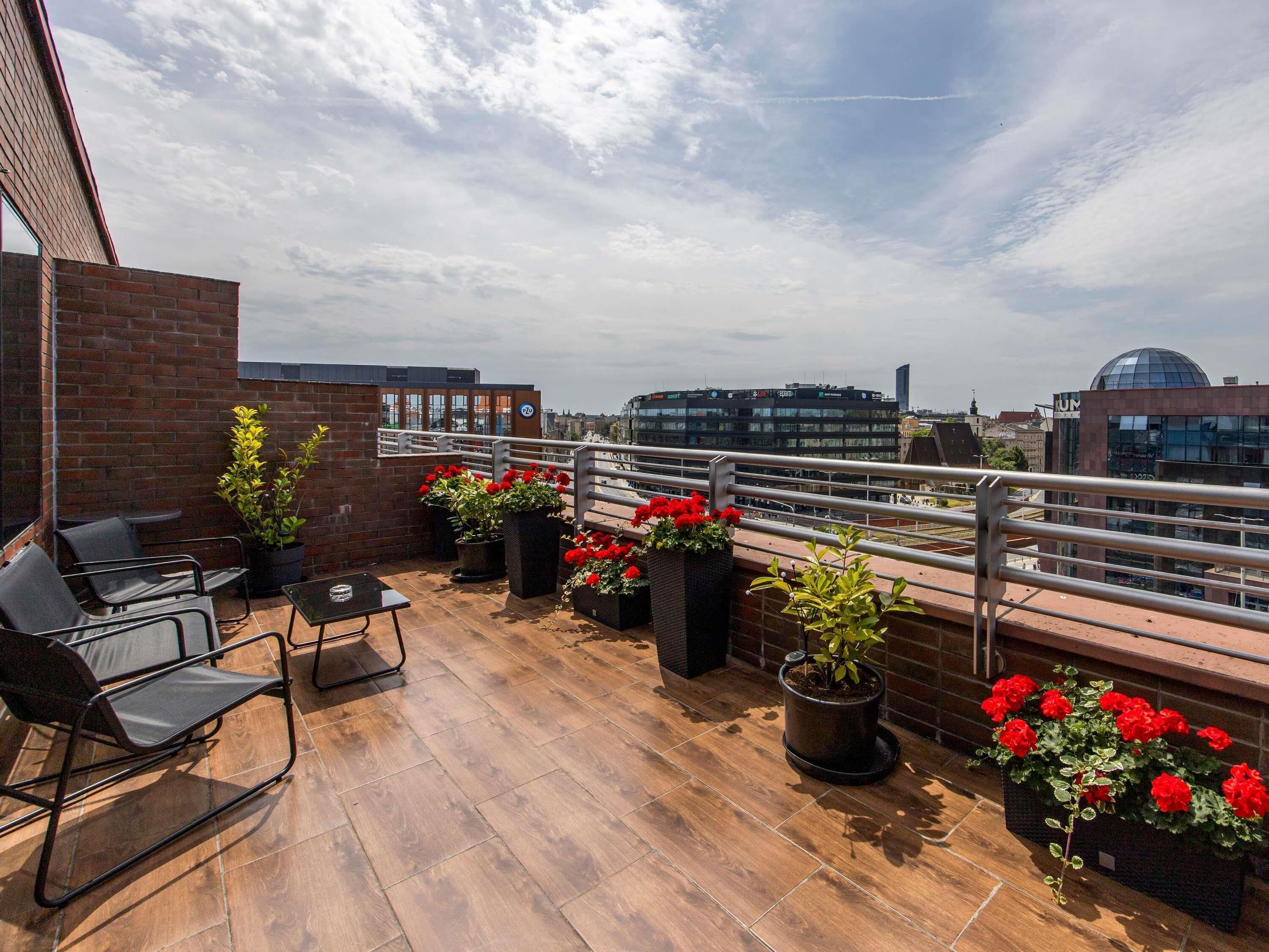 Une terrasse sur le toit, avec un mur en briques, des plantes en pot et des sièges d’extérieur.