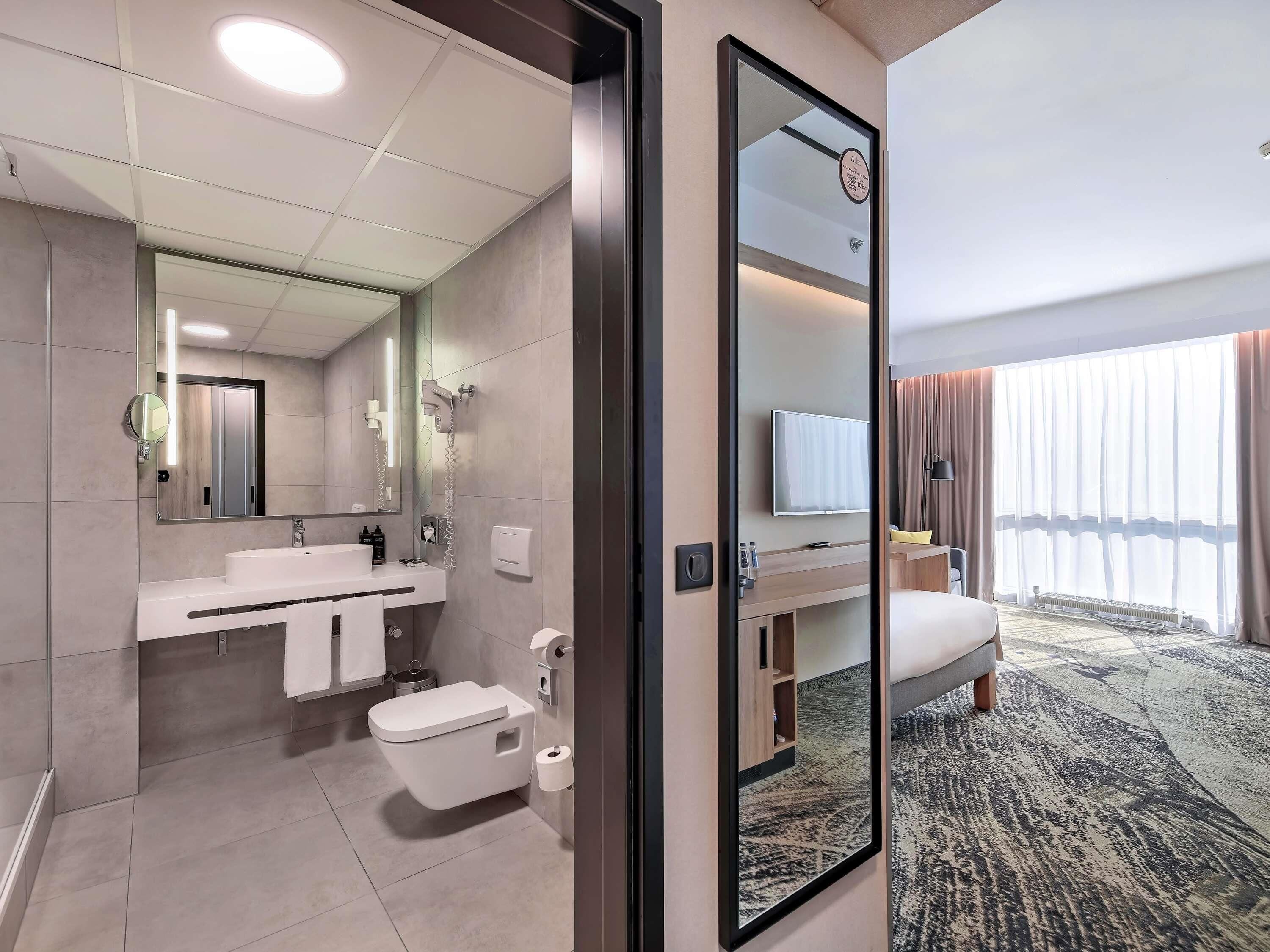 Un baño de hotel moderno con un espejo grande, un lavabo, un inodoro y una ducha.