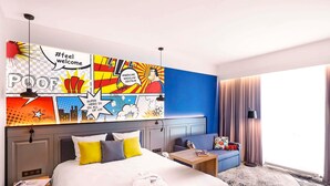 Habitación de hotel con una cama grande, un sofá y un mural colorido al estilo de cómic.