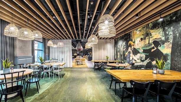 Un interior de restaurante moderno con mesas de madera, sillas negras y originales lámparas colgantes tejidas.