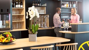 A bar area with a fruit bowl, chairs, and shelves with bottles and glasses. - Novotel Suites Paris Montreuil Vincennes (Paris)