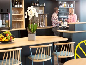 A bar area with a fruit bowl, chairs, and shelves with bottles and glasses. - Novotel Suites Paris Montreuil Vincennes (Paris)