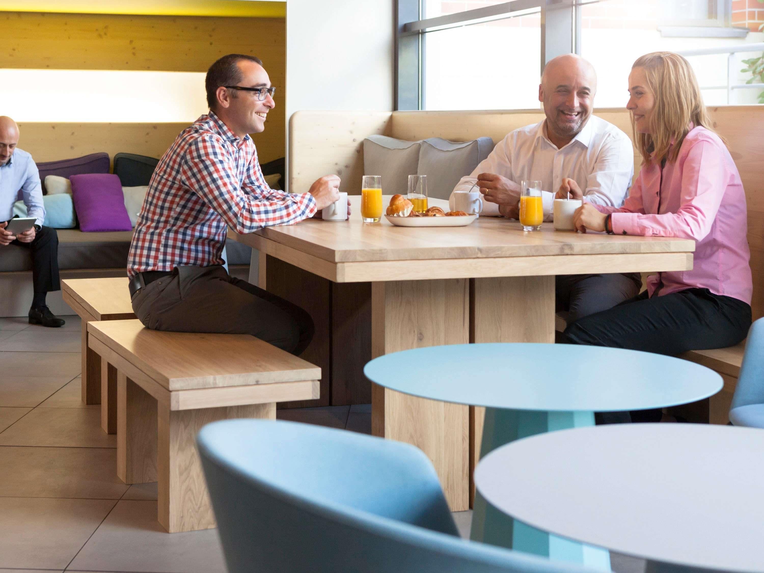 A modern cafe with wooden tables and benches, large windows, and a casual seating arrangement.