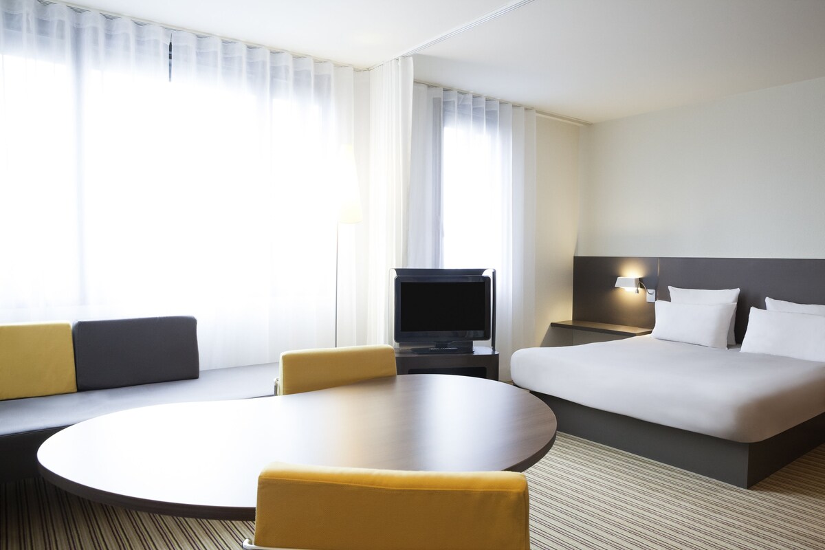 A hotel room with a bed, a TV, a sofa, a round table, and a lamp.