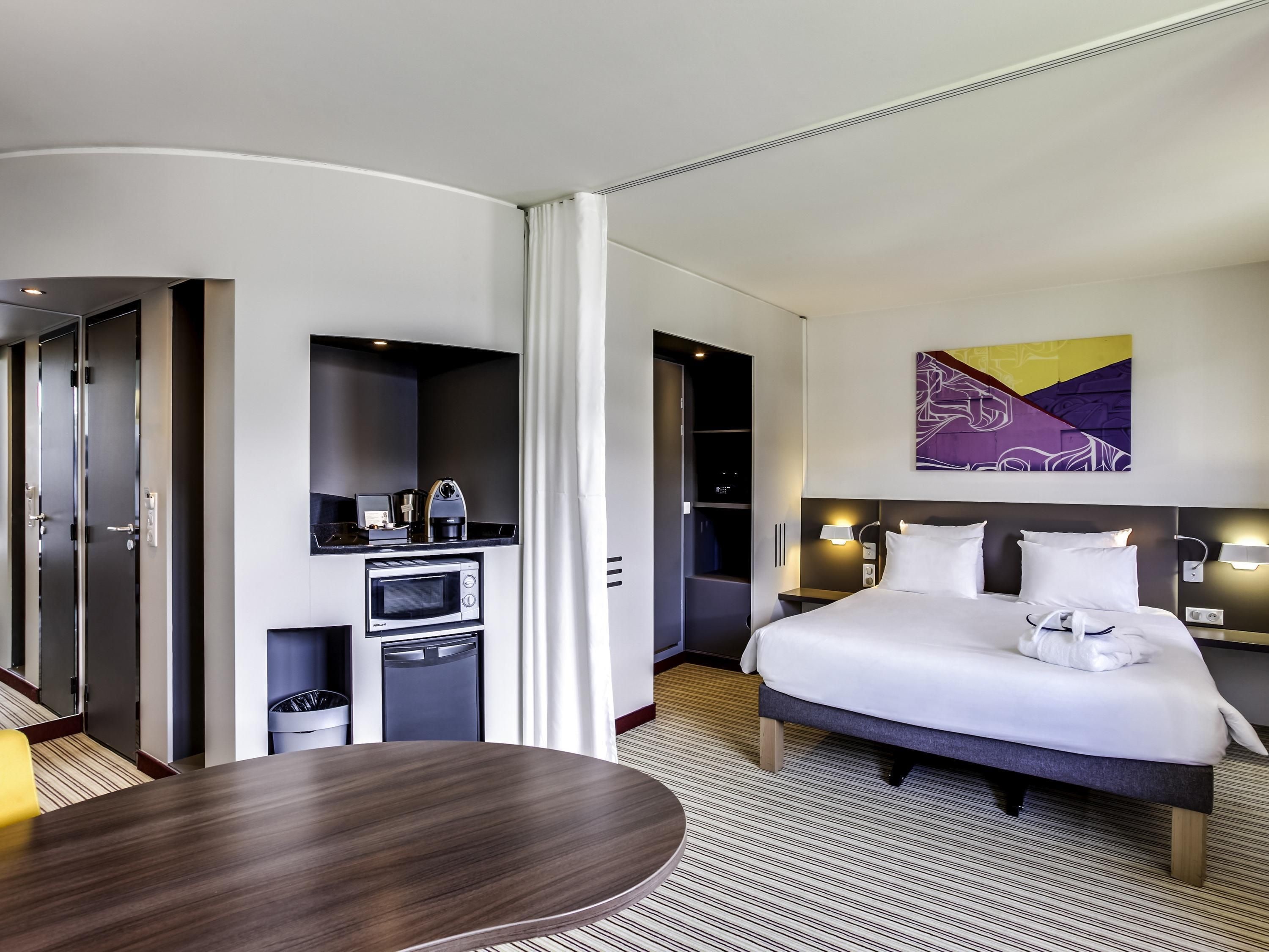 A modern hotel room with a bed, bedside table, and a built-in microwave.