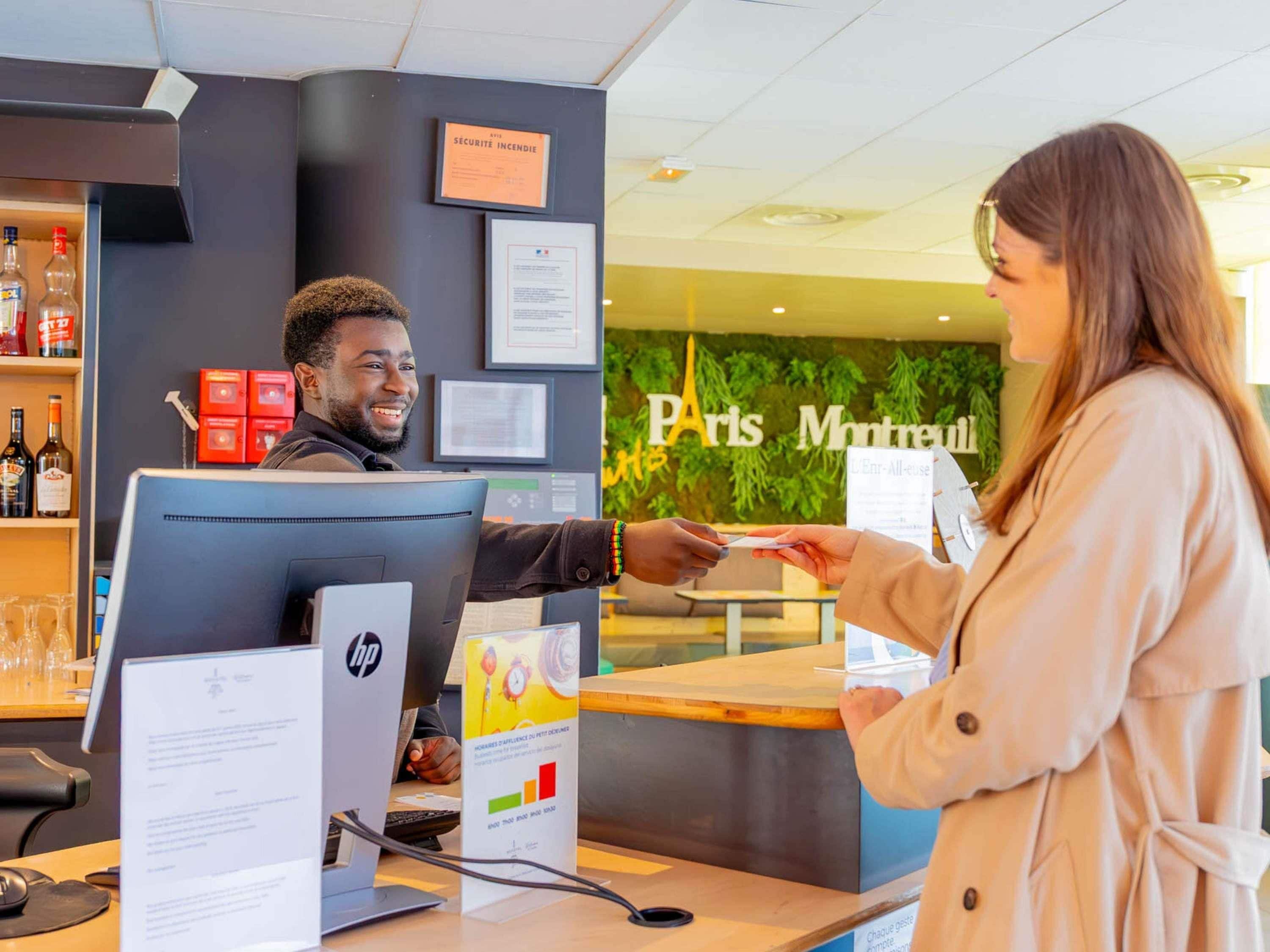 A hotel reception desk with a computer, a man behind the desk, and a woman receiving a document.