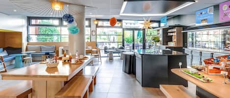 A modern cafe with wooden tables and benches, a central island with a coffee machine, and a view of greenery outside.