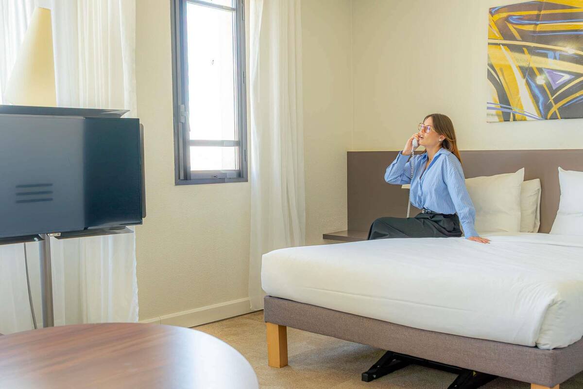 A hotel room with a bed, a television, a table, and a painting on the wall.