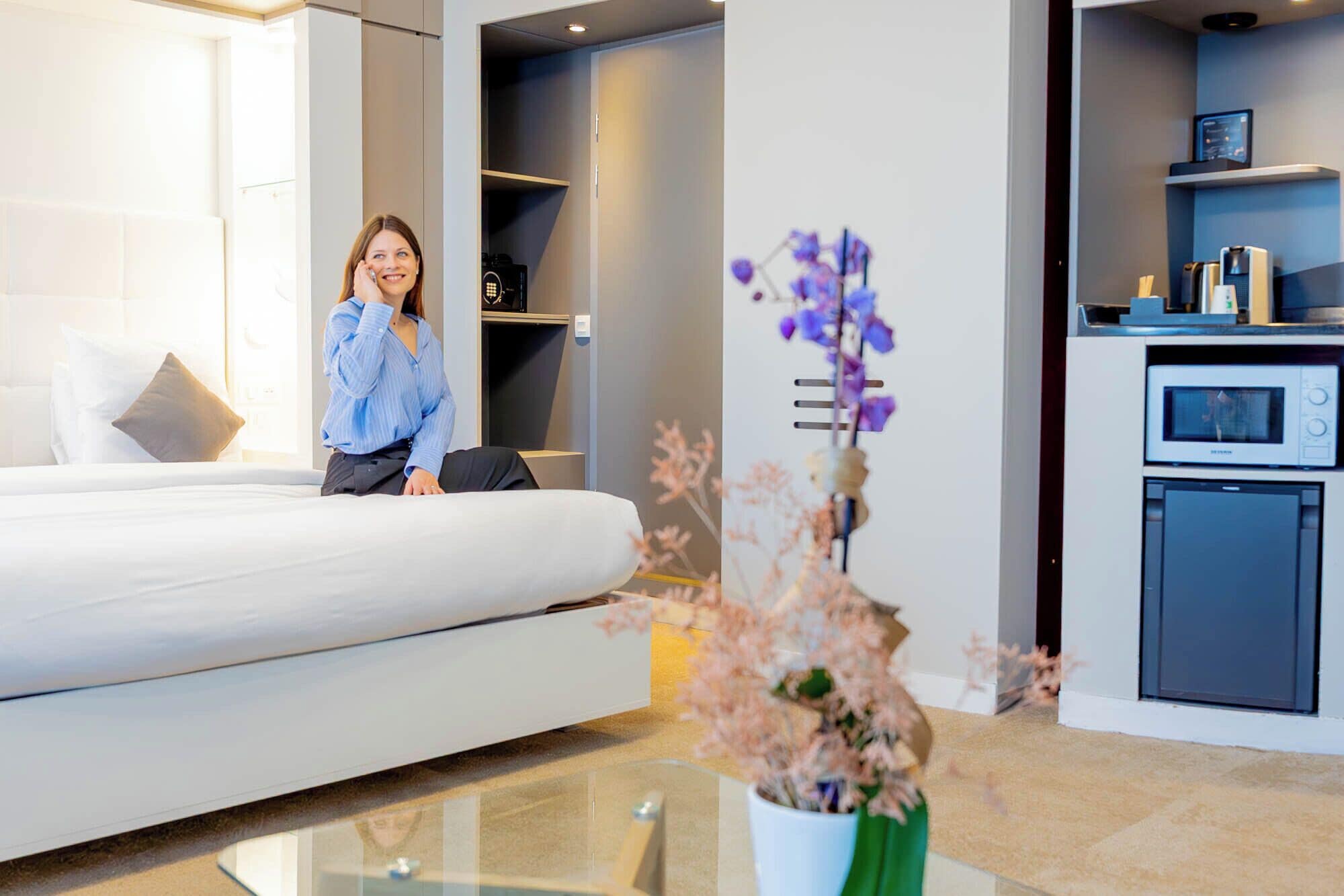 Et moderne hotelværelse med seng, et glasbord og et tekøkken.