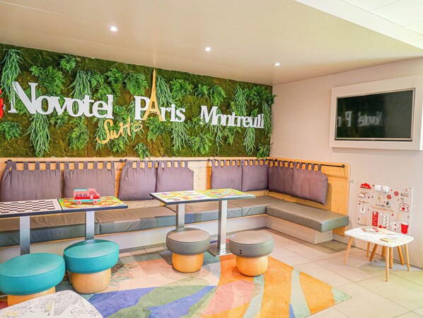 A cozy seating area with a green wall, cushioned benches, and a colorful rug. - Novotel Suites Paris Montreuil Vincennes (Paris)