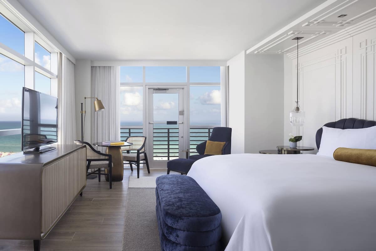 A hotel room with a large bed, a desk, a chair, and a view of the ocean.
