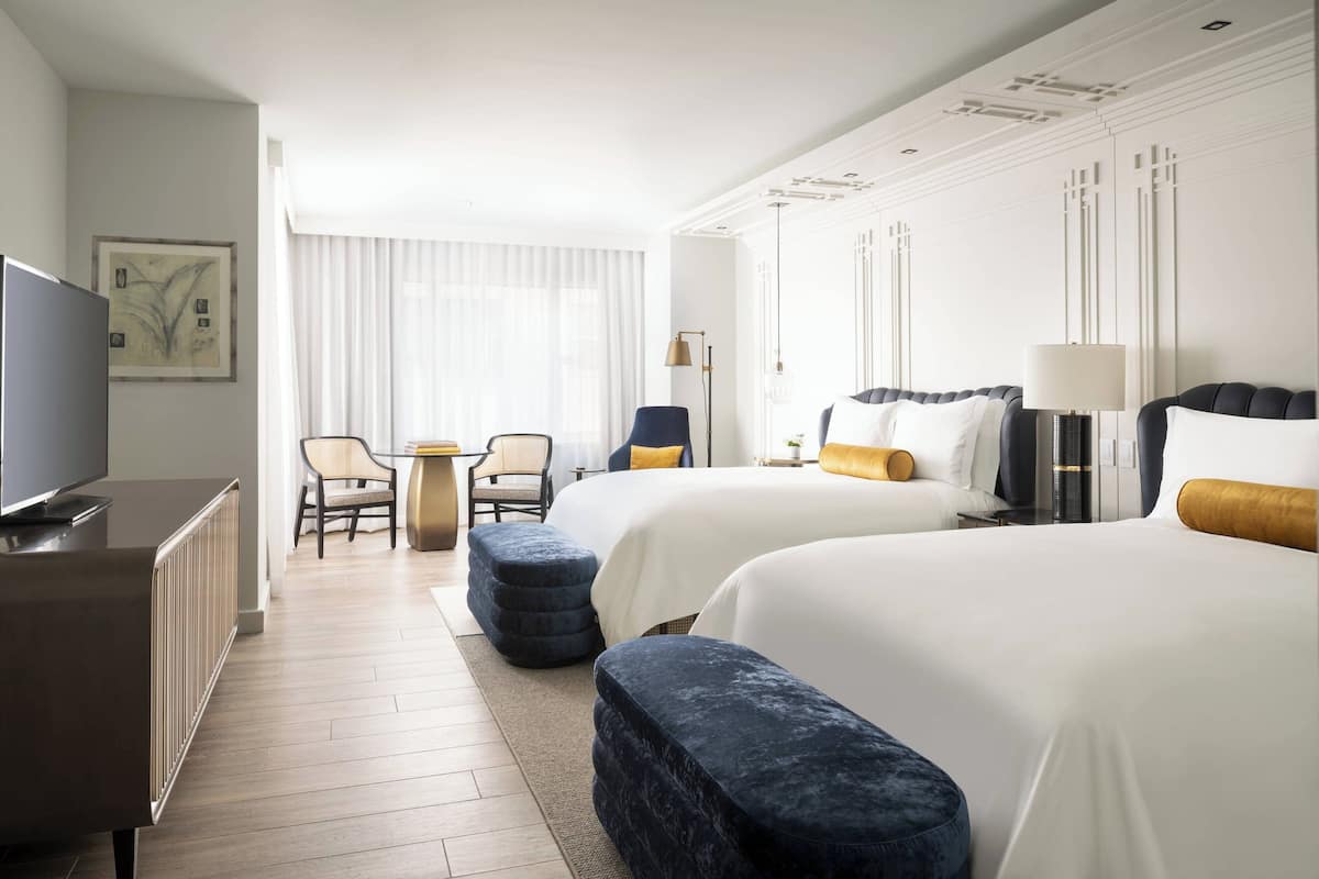A hotel room with two beds, a TV, a desk, and a chair.