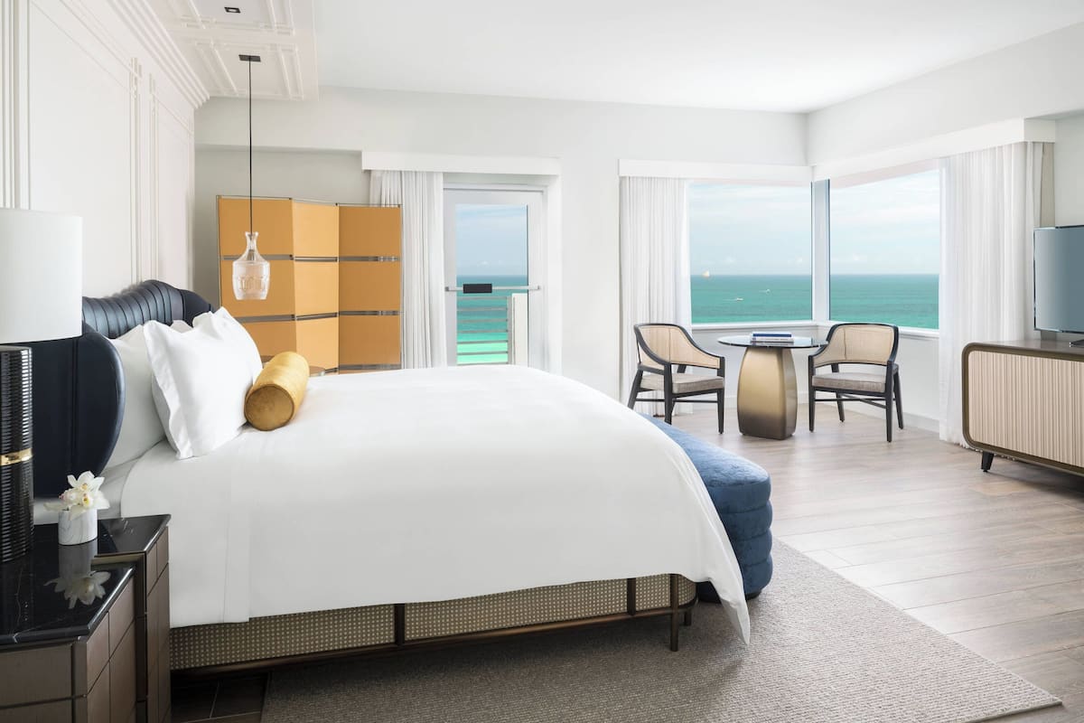 A hotel room with a large bed, a desk with a chair, a television, and a view of the ocean.
