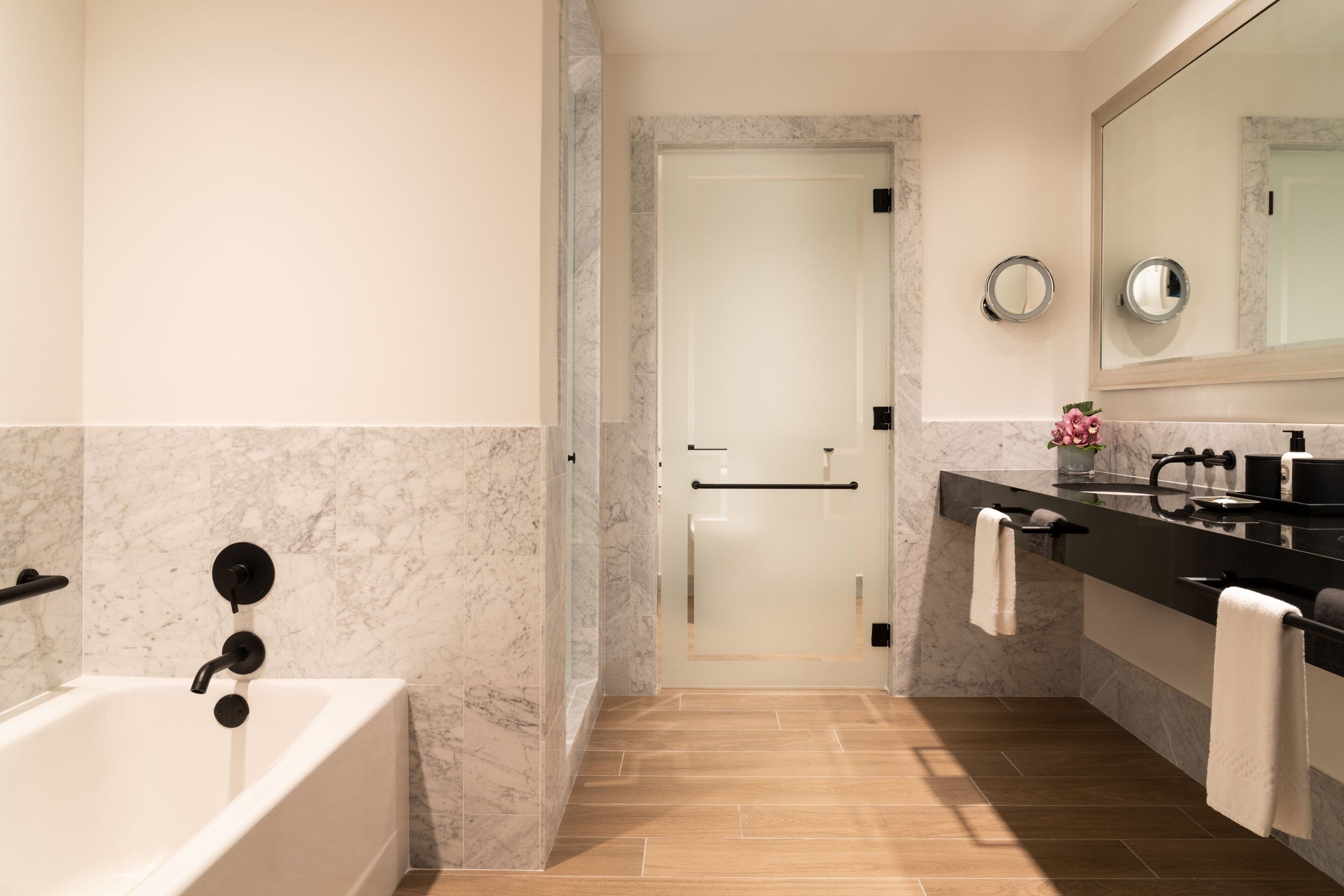Une salle de bain moderne avec une baignoire, un meuble-lavabo avec un miroir et une porte donnant sur une autre pièce.