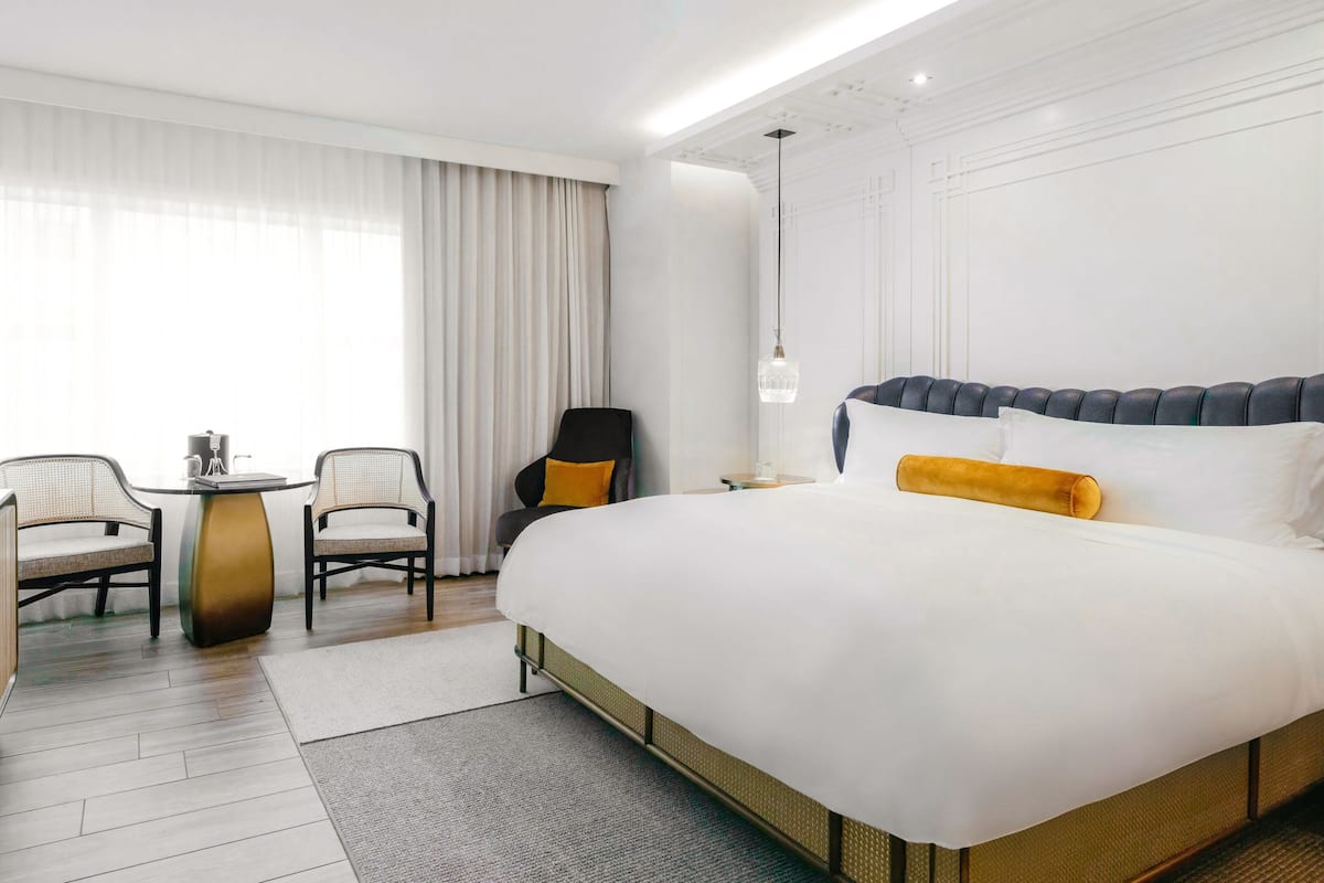 A hotel room with a large bed, two chairs, a small table, and a nightstand.