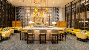 Uma área de bar com mesa de bilhar central, vários bancos e um espaço de estar com sofás e cadeiras amarelas.