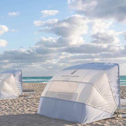 A row of white beach tents on a sandy beach with the ocean in the background.