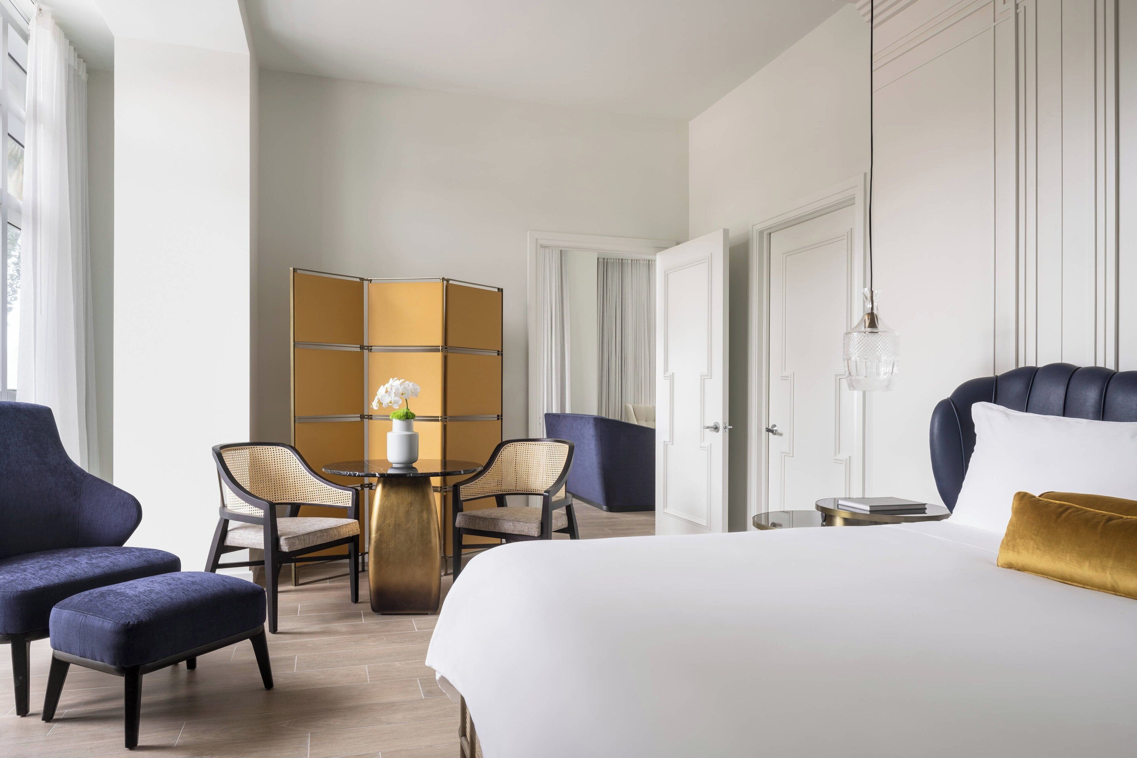 Une chambre d’hôtel avec un grand lit, deux fauteuils, une petite table ronde et un coin salon avec des chaises et un canapé.