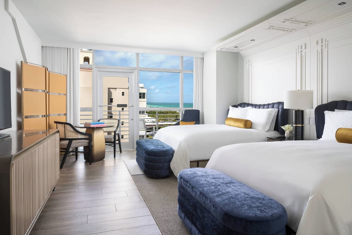 A hotel room with two beds, a desk, and a view of the ocean.