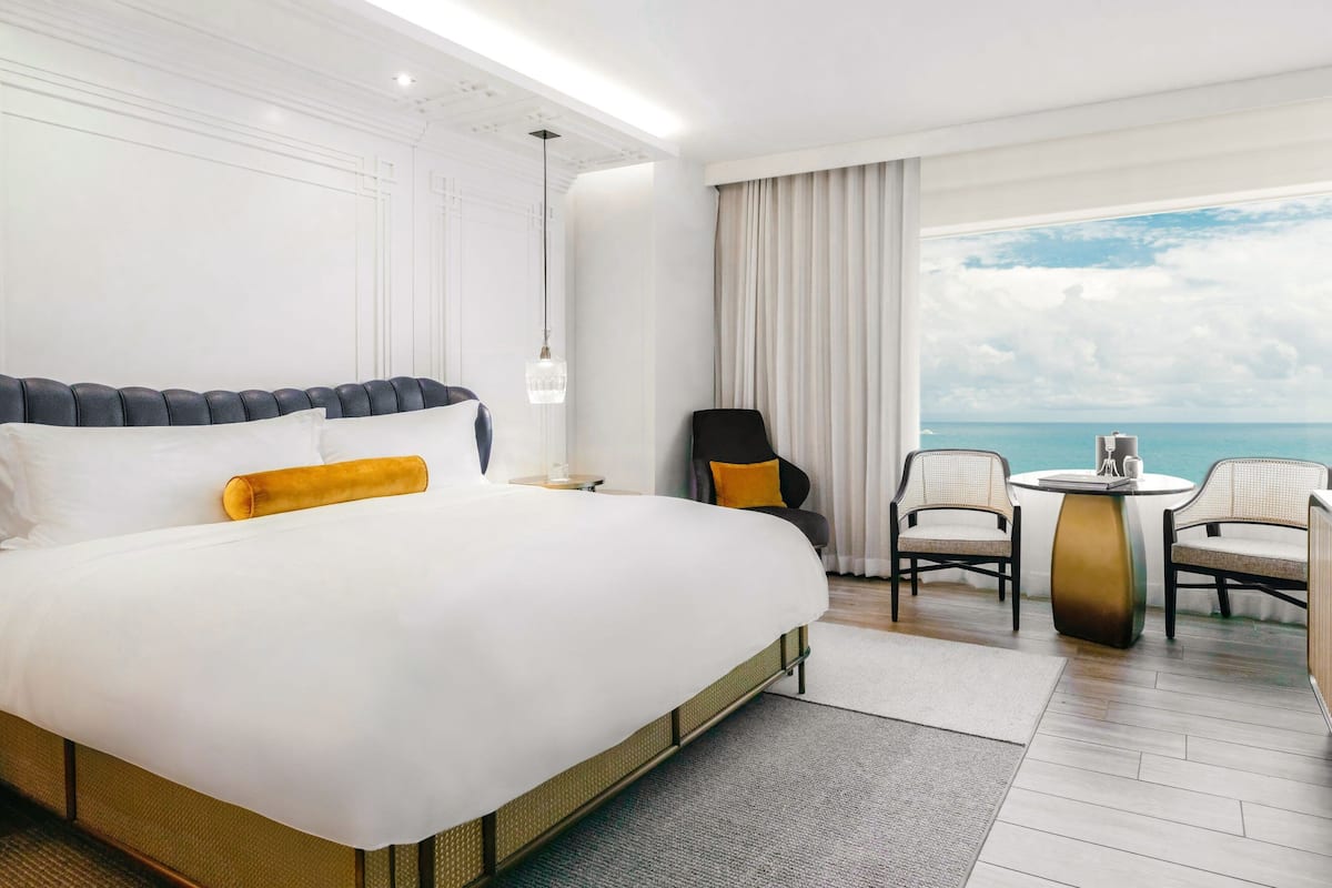 A hotel room with a large bed, a round table, two chairs, and a view of the ocean.