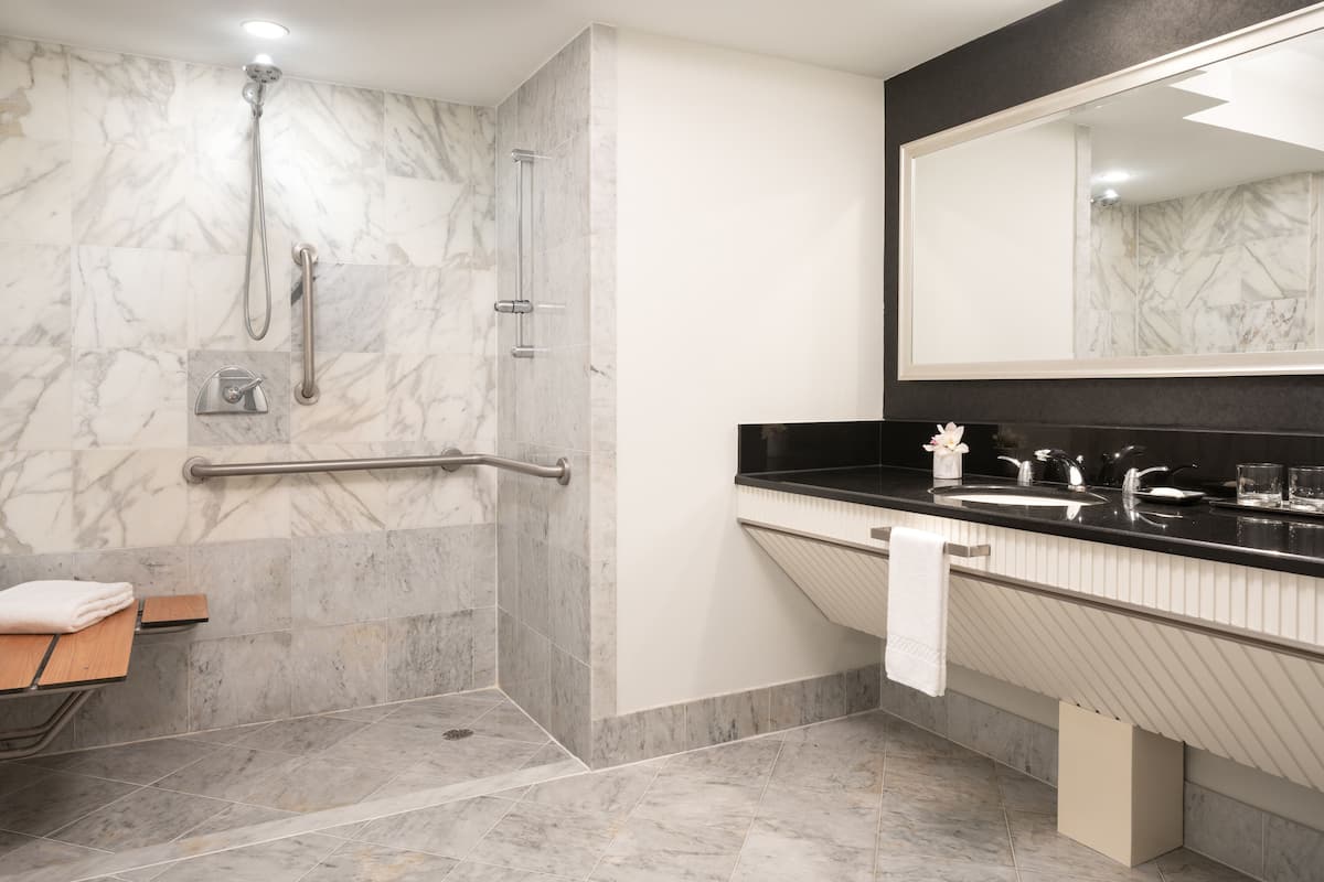 A modern bathroom with a walk-in shower, grab bars, a vanity with a black countertop, and a large mirror.