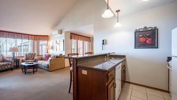 A spacious living room with a sofa, chairs, and a coffee table. There is a kitchen area with a sink and cabinets.