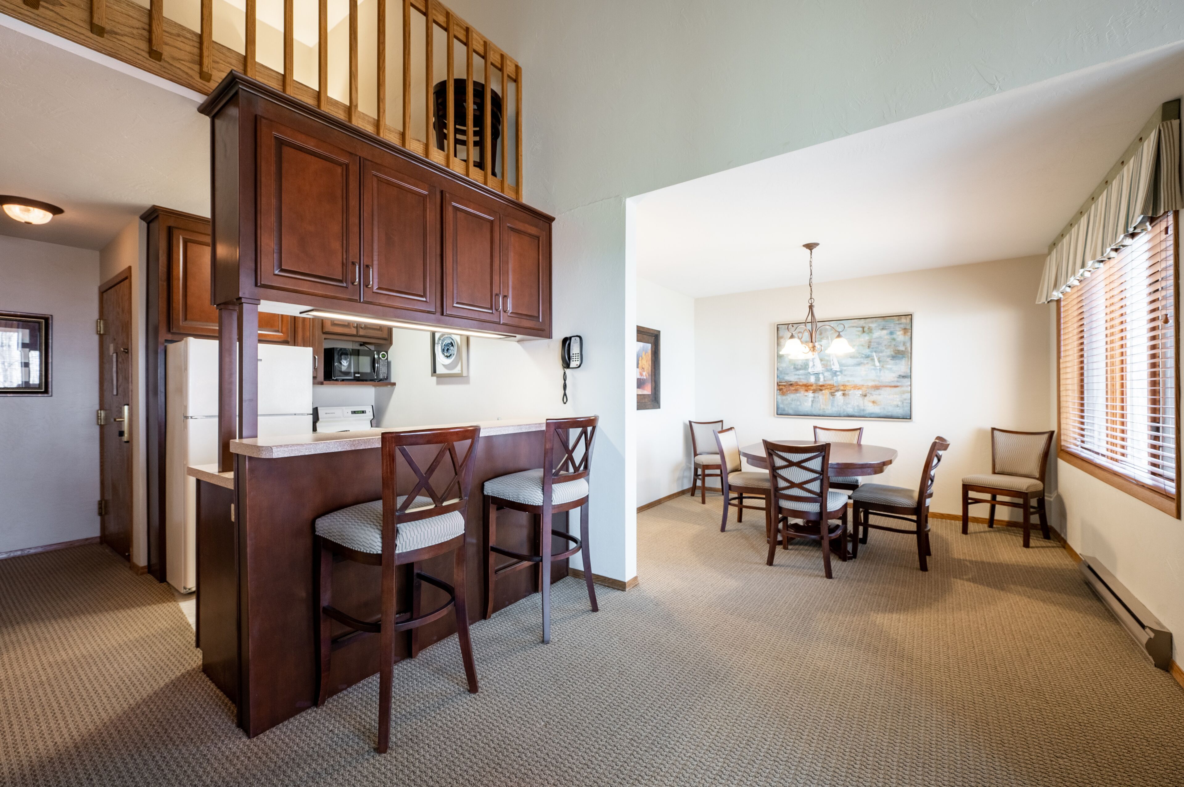 A kitchen with dark wooden cabinets, a microwave, and a refrigerator. There is a dining area with a table and chairs.