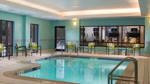 An indoor swimming pool with clear water, surrounded by green chairs and exercise equipment. - Springhill Suites By Marriott Chicago Lincolnshire (Lincolnshire)