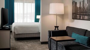 A hotel room with a bed, a sofa, a desk, a lamp, and a cityscape painting. - Springhill Suites By Marriott Chicago Lincolnshire (Lincolnshire)