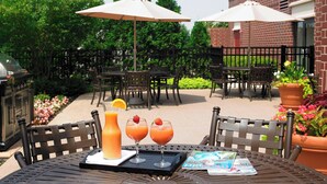 An outdoor patio with a grill, two umbrellas, and a table with drinks and a magazine. - Springhill Suites By Marriott Chicago Lincolnshire (Lincolnshire)