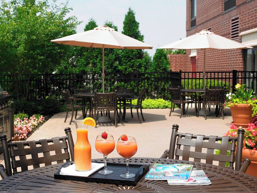 An outdoor patio with a grill, two umbrellas, and a table with drinks and a magazine.