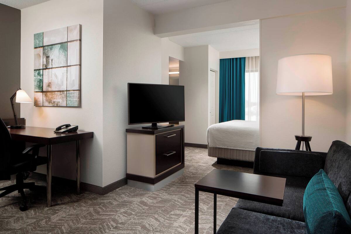 A hotel room with a desk, television, bed, and a lamp.