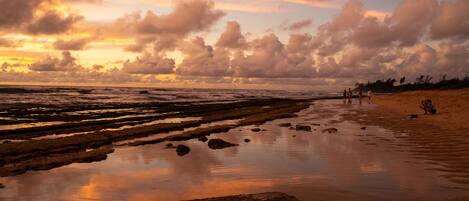 A beach with a sunset, rocky shoreline, and people walking.