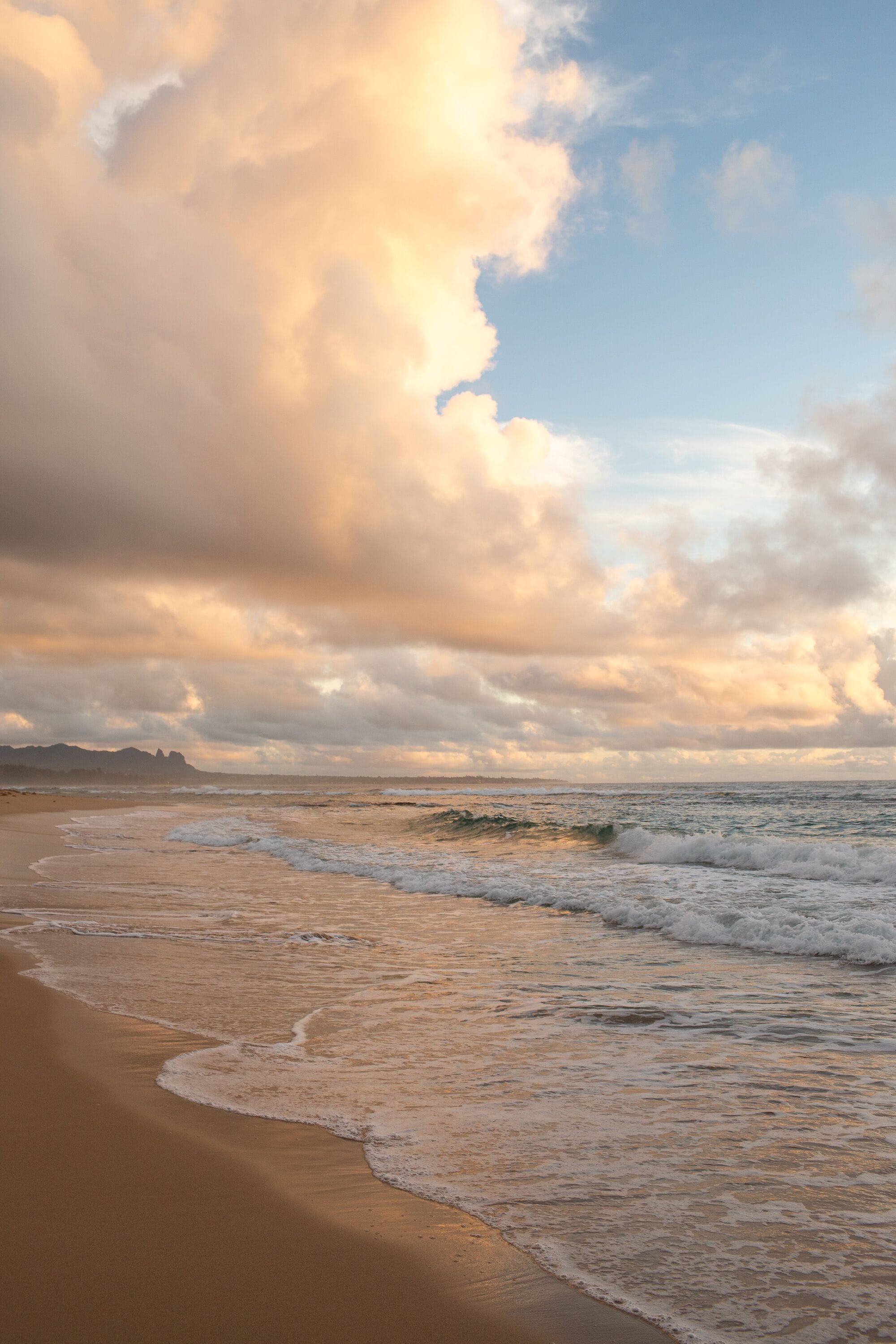 A beach with waves gently lapping onto the shore under a partly cloudy sky.