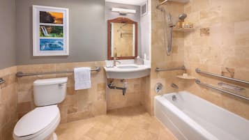 Une salle de bain équipée de toilettes, d’un lavabo, d’une baignoire et d’une douche. On y trouve également des barres d’appui et un porte-serviettes.