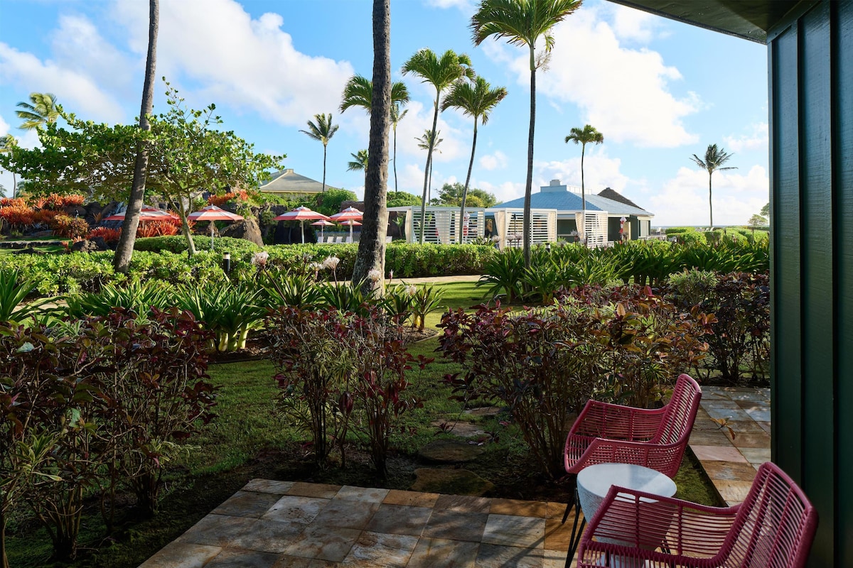 A patio with red chairs and a stone pathway leading to a building with a blue roof.