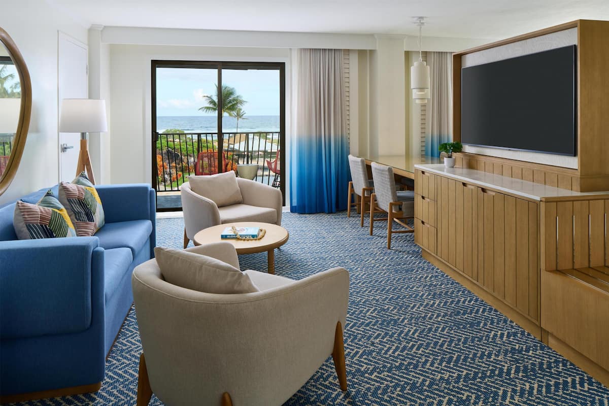 A hotel room with a balcony, a TV, a sofa, a chair, and a small table.