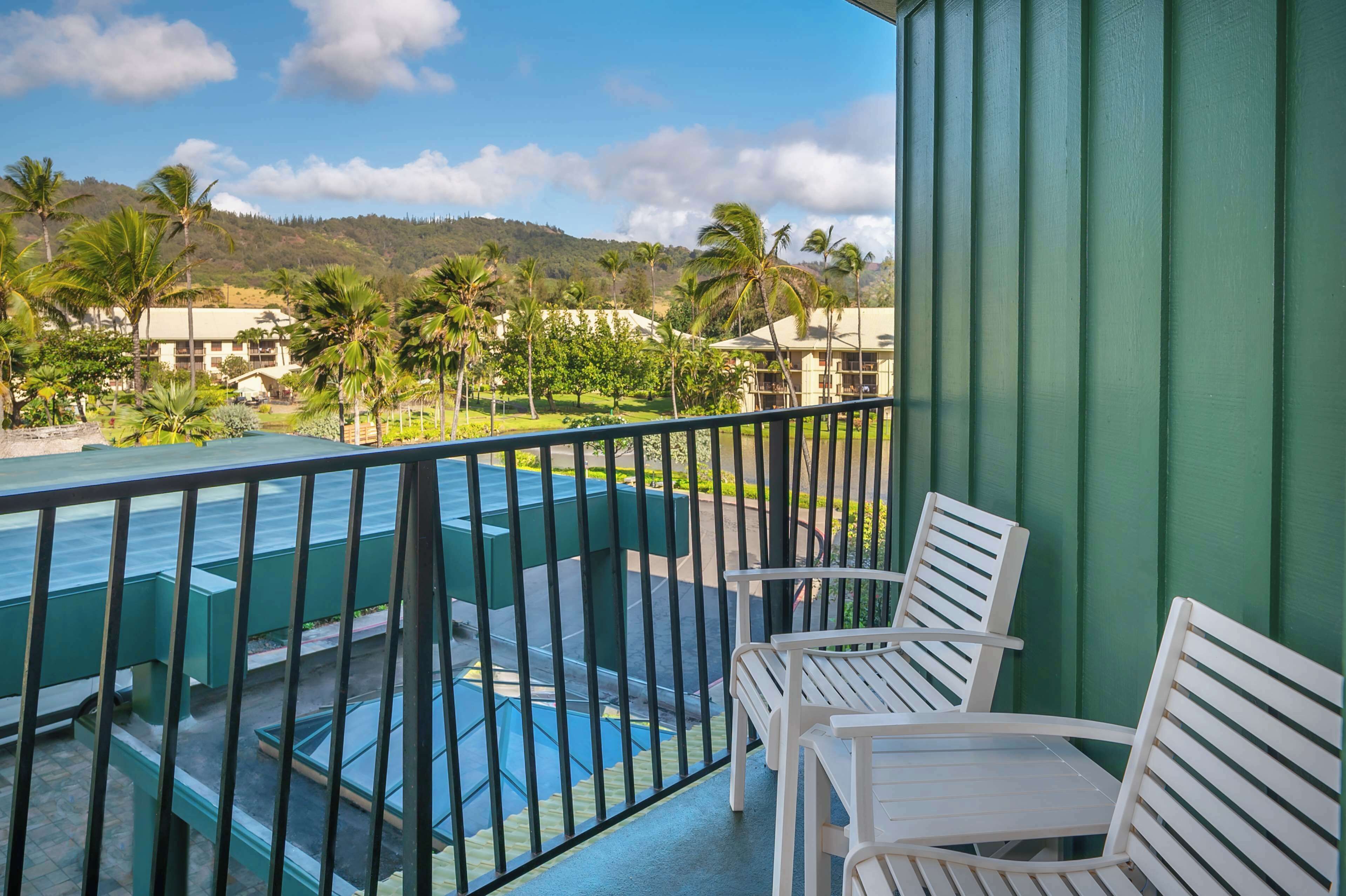 Un balcon donnant sur une piscine et des palmiers, avec des chaises blanches et un mur végétal.